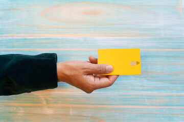 Top view of woman hand holding a yellow debit card with contact less on blue stripped wood background