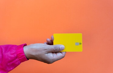 Top view of young hand taking yellow debit card with contact less symbol on orange background card purchasing concept