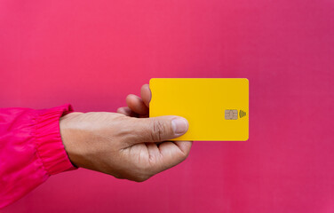 Close up seen from above of young woman hand holding yellow credit card on fuchsia background