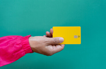 Young woman hand holding yellow credit card seen from above with green backgroun
