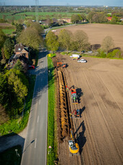 Aerial view of road construction site next to stretch of farmland. Workers, heavy machinery,...