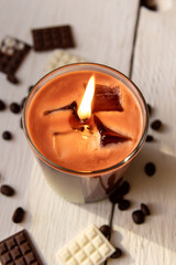 Gel candle in glass cup. A trend candle in the form of iced coffee. Lighted candle on white wooden background