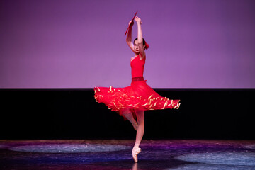 ballerina in a red dress performs a variation from the ballet Don Quixote on the theater stage.