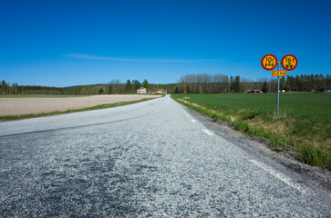 Asphalt road leading among fields to farm houses in Sweden on sunny day, Road prohibitory signs round with yellow background and red border No vehicles exceeding weight