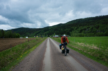 Cyclist on touring bicycle with bags solo travel in Sweden, Nordic countryside, Overcast weather, Long distance cycling travel around the world