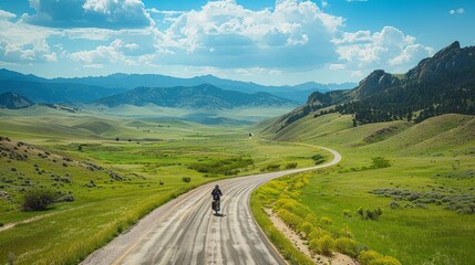 Fototapeta premium A man is riding a bicycle down a road in the mountains