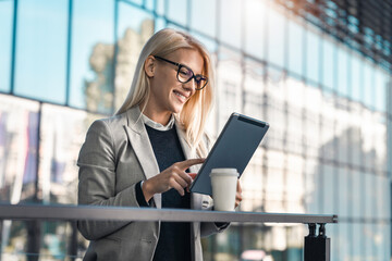 Happy smiling businesswoman using digital tablet while standing on the balcony of an office building.
