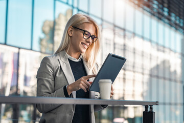 Happy smiling businesswoman using digital tablet while standing on the balcony of an office...