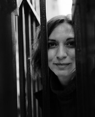 Monochrome head-shot of woman looking at camera though bars.
