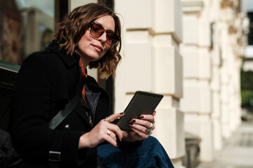 Woman sitting in a street reading an e-book in a sunny day.