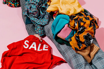 man covered by a pile of clothes grabs a shirt with the word sale