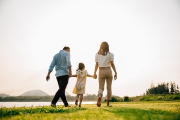 Happy Asian family walking and playing together in a beautiful nature setting, with green grass and...