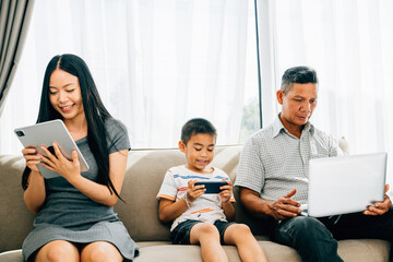 An Asian family at home fixated on gadgets disregards togetherness. Parents and kids absorbed in...