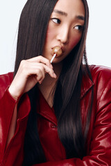 Attractive woman with long black hair and red jacket enjoying a piece of candy in her mouth