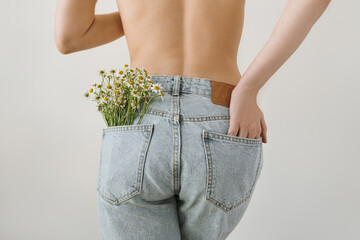 Young pretty woman with chamomile flowers bouquet in jeans pocket. Backside view