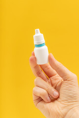 A hand is holding a white plastic medical bottle with a white and blue cap