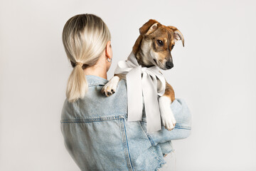 Blond woman in casual clothing standing with her back and holding young adorable dog with a white...