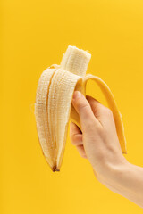 A hand holds a peeled banana on a yellow background