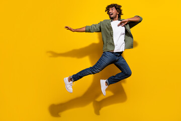 Portrait photo of young funny mexican guy in khaki shirt and jeans jumping making dab gesture...