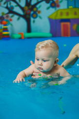 A little 8-month-old boy is learning to swim in the pool with a coach.