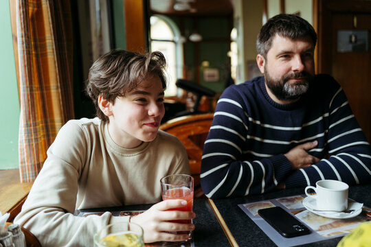 Smiling man and kid sitting closely at dining table.