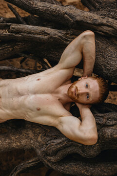Redhead nude Man bare-chested athlete posing near tree roots outside