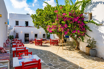 Typical Greek taverna restaurant with red chairs and bougainvillea flowers on square in Apollonia...