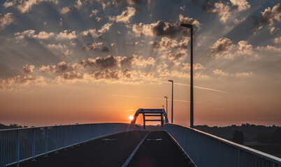 wschodzące słońca za drogą i mostem z pięknymi promieniami słońca wśród chmur © Henryk Niestrój