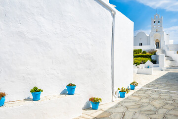 Blue flower pots on courtyard of Chrysopigi monastery and beautiful white church in background, Sifnos island, Greece