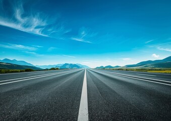 A wide highway with a blue sky and white clouds in the background. Green mountains on both sides of the road with trees growing along each side