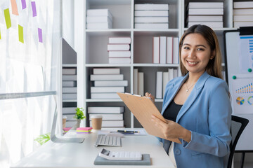 Asian businesswoman sits behind a desk looking at a monitor with a stock market graph tracking market prices. Big data analysis helps business in modern business office