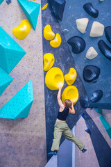Bouldering climbing athlete woman training at indoor gym boulder climb wall. Teenager fit girl...