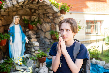11 year old Catholic boy prays to God in front of a statue of the Virgin Mary