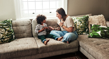 Mother, child and stethoscope on sofa for fun, heartbeat and playful together in living room. Mom,...