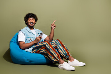 Full length photo of nice young male sit beanbag device point empty space dressed stylish denim...