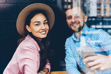 Romantic couple sitting at table in cafe during date posing for selfie on smartphone camera, hipster guy resting together with girlfriend using telephone for making picture for share in networks
