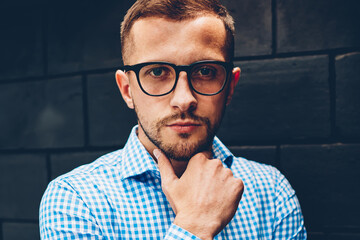 Half length portrait of handsome male entrepreneur in eyeglasses in casual wear posing near wall indoors, handsome confident businessman looking at camera concentrated on ideas for new startup project