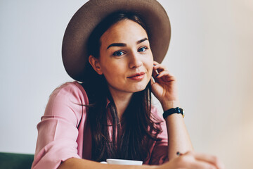 Portrait of attractive hipster girl in trendy hat making notes in diary resting in cozy interior coffee shop,young pretty woman looking at camera enjoying free time and creating ideas for startup