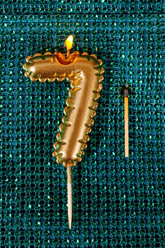 lit golden candle in the shape of the number 7
