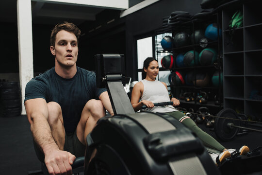 Strong young athletes exercising with rowing machine while in gym