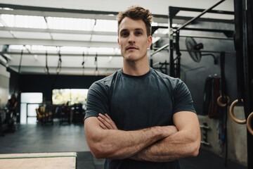 Confident young man standing with arms folded in gym