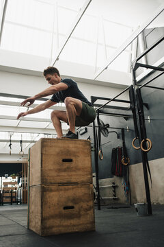 Fit man box jumping in crossfit gym