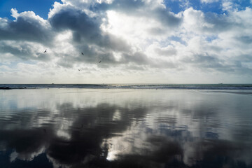 Les nuages et le ciel se reflètent harmonieusement sur le sable mouillé d'une plage de la presqu'île de Crozon, créant une atmosphère paisible à marée basse.