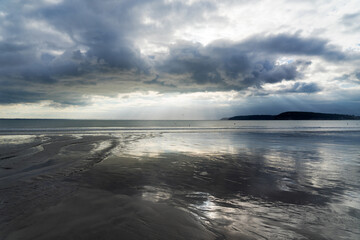Les nuages gris se miroitent sur le sable humide d'une plage de la presqu'île de Crozon, ajoutant...