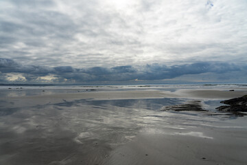 De beaux reflets des nuages sur le sable mouillé d'une plage de la presqu'île de Crozon, sous un ciel parsemé de quelques nuages blancs à marée basse.