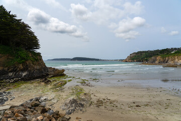 Une plage de la presqu'île de Crozon, entourée de falaises, s'étend sous un ciel parsemé de quelques nuages blancs à marée basse.