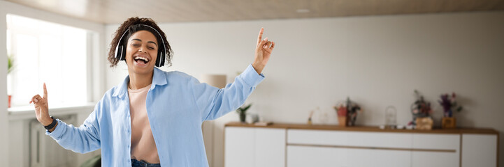 Taking Break. Overjoyed millennial black woman wearing wireless headphones dancing, having fun...