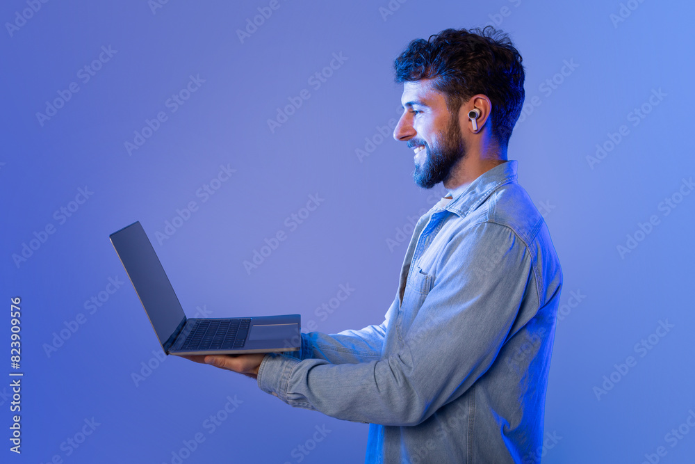 Aufkleber A man with a beard is standing while holding a laptop in his hands. He appears to be looking at the screen intently, possibly working or browsing the internet.