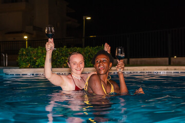 Tipsy girls dancing in the swimming pool holding wine glasses.