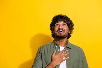 Portrait photo of young mexican guy in khaki shirt thankful touching heart look up for god support isolated on yellow color background